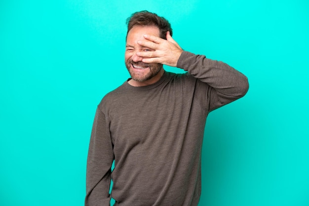 Middle age caucasian man isolated on blue background covering eyes by hands and smiling