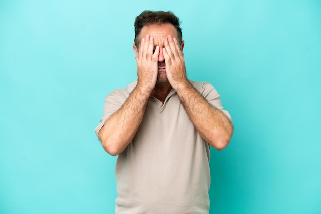 Middle age caucasian man isolated on blue background covering eyes by hands