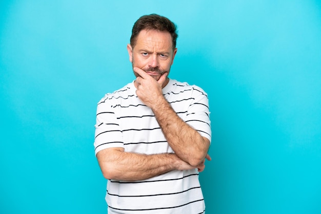 Middle age caucasian man isolated on blue background having doubts