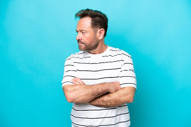 Middle age caucasian man isolated on blue background keeping the arms crossed