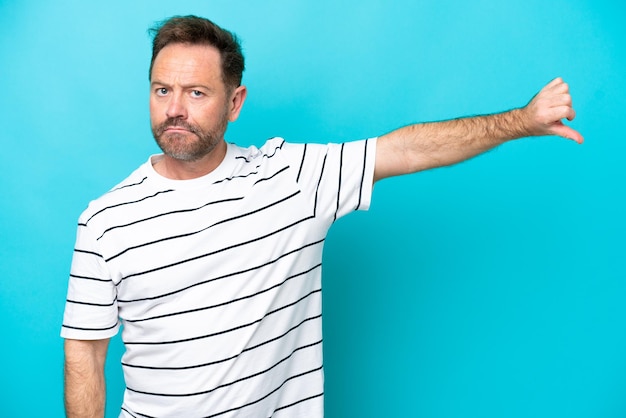 Middle age caucasian man isolated on blue background showing thumb down with negative expression