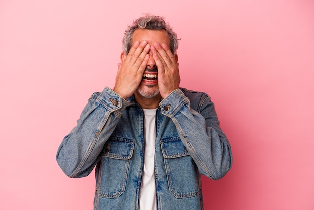 Middle age caucasian man isolated on pink background  covers eyes with hands, smiles broadly waiting for a surprise.