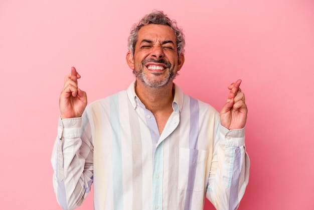 Middle age caucasian man isolated on pink background crossing fingers for having luck