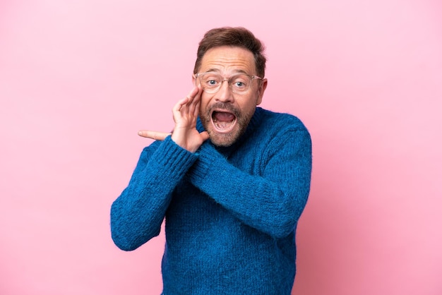 Middle age caucasian man isolated on pink background pointing to the side to present a product and whispering something