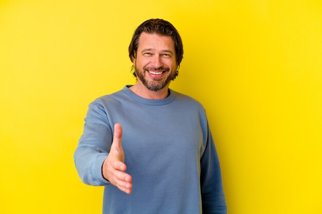 Middle age caucasian man isolated on yellow wall stretching hand in greeting gesture.