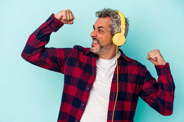 Photo middle age caucasian man listening to music isolated on blue background raising fist after a victory winner concept