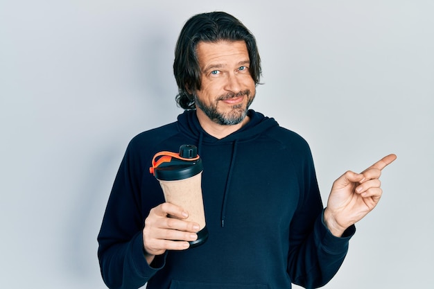 Middle age caucasian man wearing sport clothes drinking a protein shake smiling happy pointing with hand and finger to the side