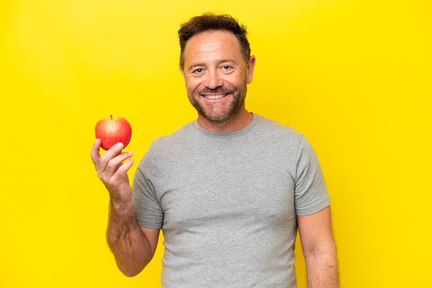 Middle age caucasian man with an apple isolated on yellow background smiling a lot