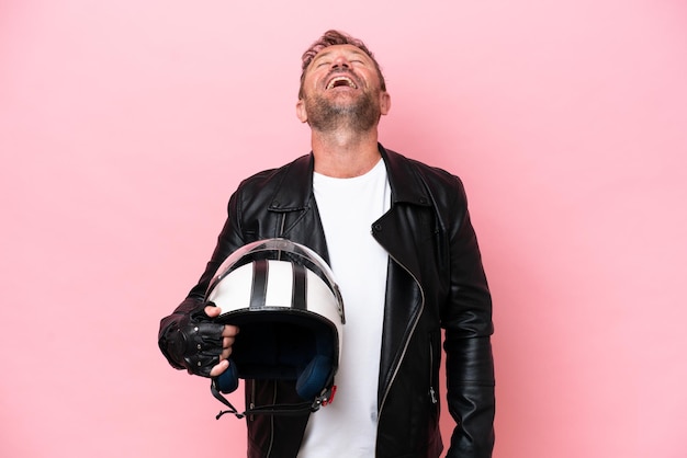 Middle age caucasian man with a motorcycle helmet isolated on pink background laughing