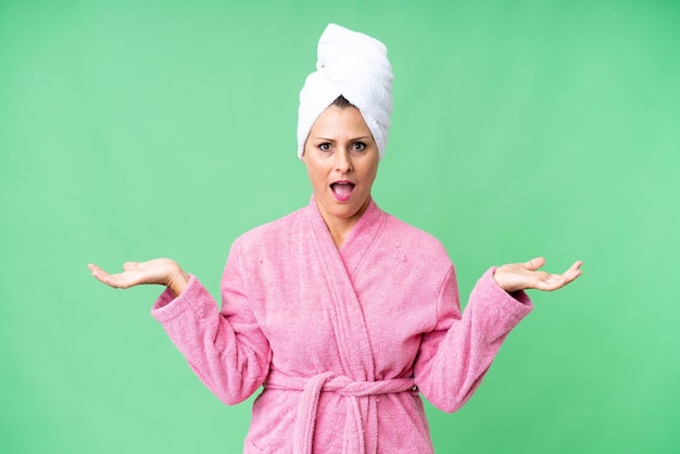 Middle age caucasian woman in a bathrobe over isolated background with shocked facial expression