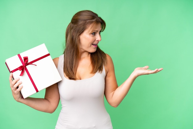 Middle age caucasian woman holding a gift over isolated background with surprise facial expression