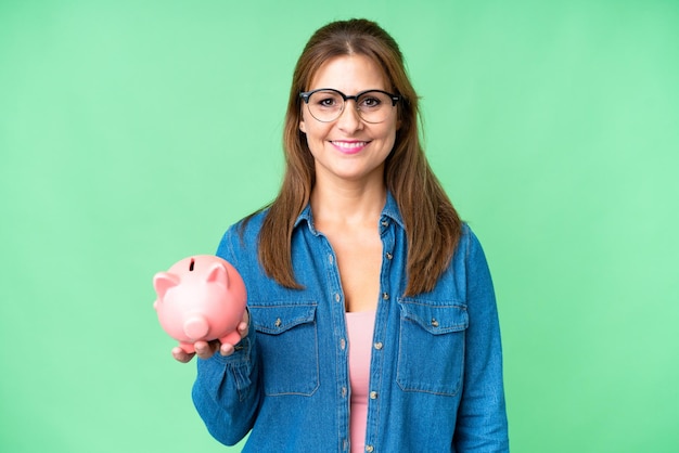 Middle age caucasian woman holding a piggybank over isolated background smiling a lot