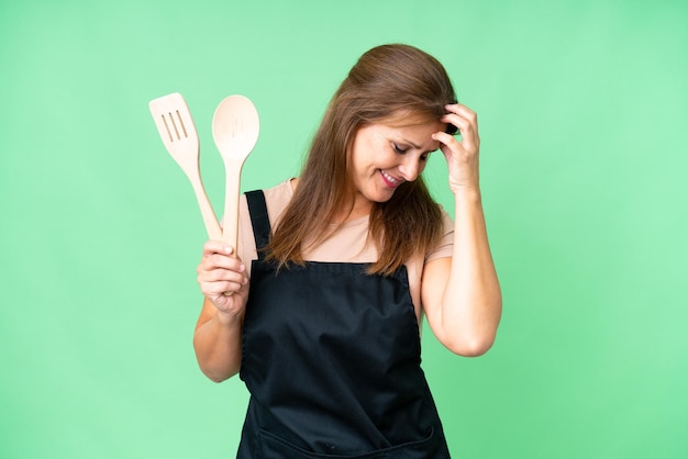 Middle age caucasian woman holding a rolling pin over isolated background laughing