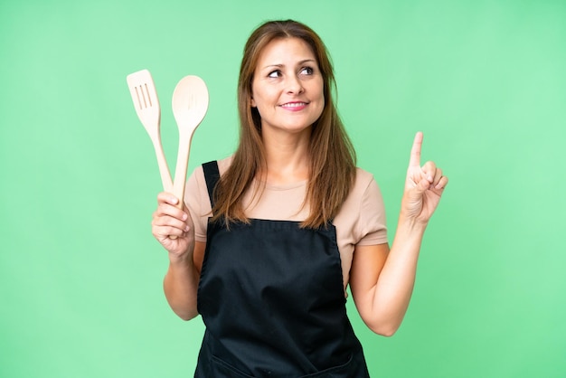 Middle age caucasian woman holding a rolling pin over isolated background pointing up a great idea