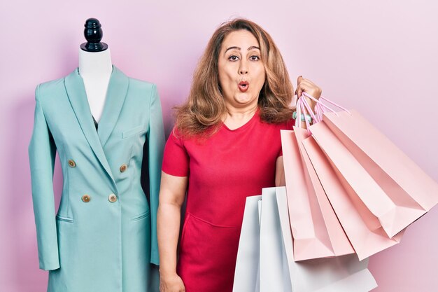 Middle age caucasian woman holding shopping bags scared and amazed with open mouth for surprise disbelief face