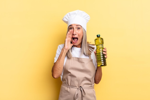 Middle age chef woman feeling happy, excited and positive, giving a big shout out with hands next to mouth, calling out