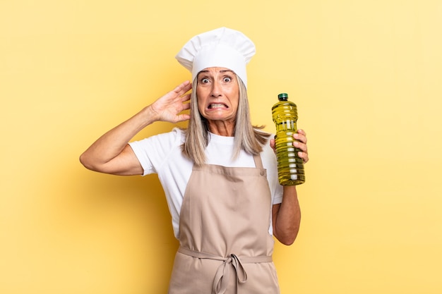 Middle age chef woman feeling stressed, worried, anxious or scared, with hands on head, panicking at mistake