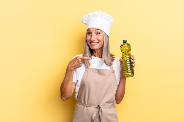 Middle age chef woman smiling cheerfully, feeling happy and pointing to the side and upwards, showing object in copy space