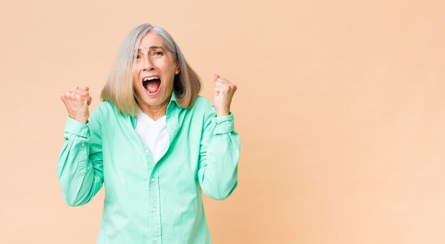 Middle age cool woman shouting aggressively with an angry expression or with fists clenched celebrating success