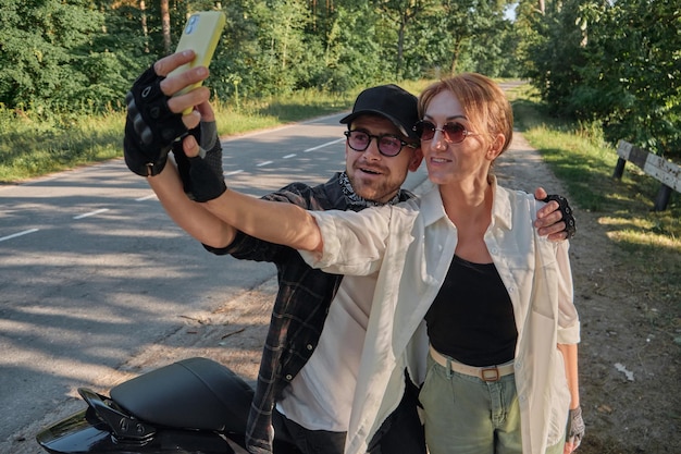 Middle age couple riding a motorcycle having fun and taking a selfie on a mobile phone camera