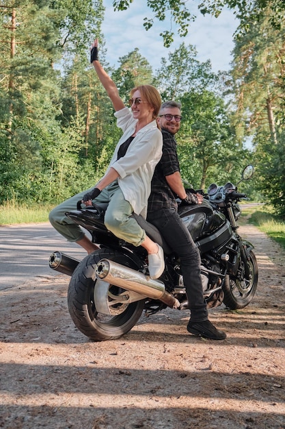 Middle age couple talking and having fun sitting on a motorcycle traveling together on a forest road