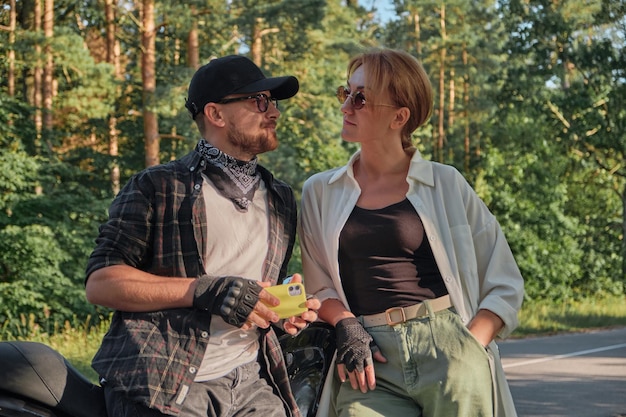 Middle age couple talking sitting on a motorcycle traveling together on a forest road