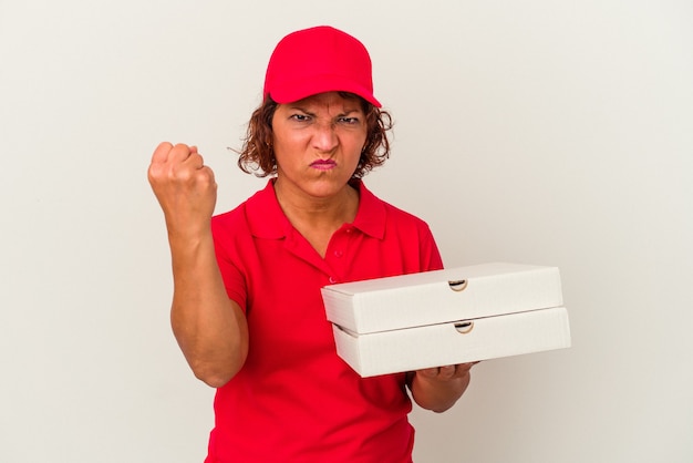 Middle age delivery woman taking pizzas isolated on white background showing fist to camera, aggressive facial expression.