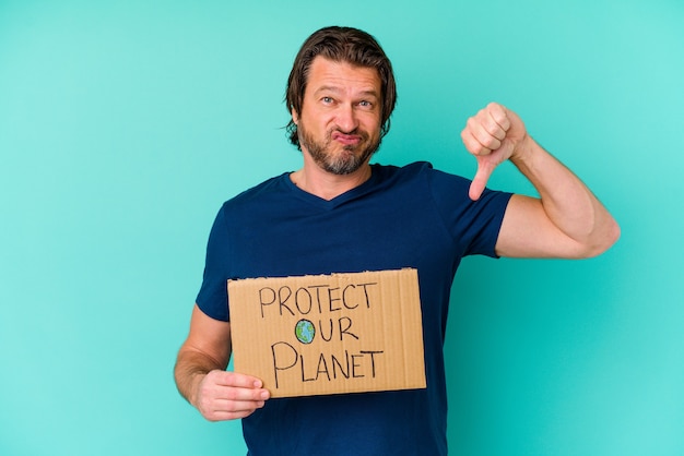 Middle age dutch man holding a protect our planet placard isolated on blue wall showing a dislike gesture, thumbs down. Disagreement concept.