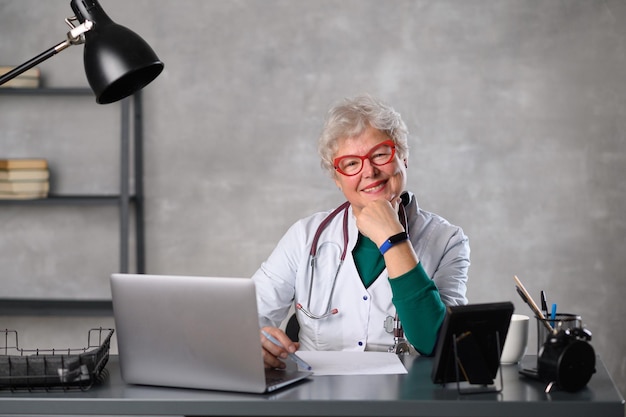 Middle age female doctor using laptop, writing notes with stethoscope on table. Healthcare concept. Medical doctor writing and taking notes.