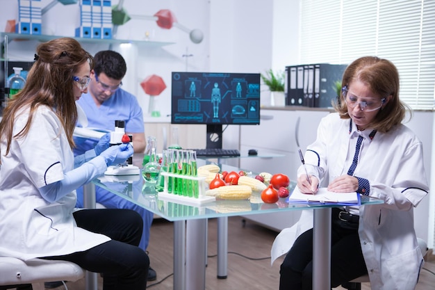 Middle age female scientist making notes after a product test on strawberries. Test tubes.