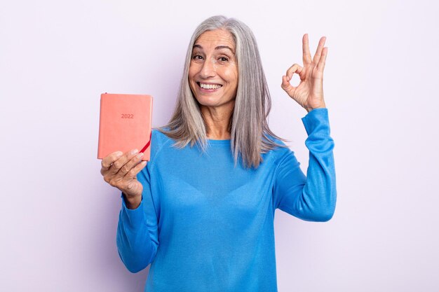 Middle age gray hair woman feeling happy, showing approval with okay gesture. 2022 agenda concept