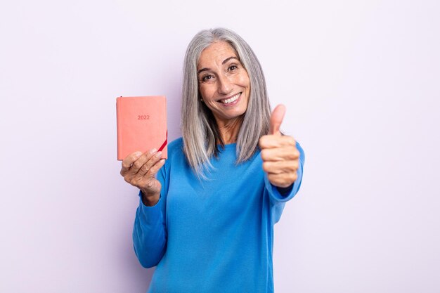 Middle age gray hair woman feeling proud,smiling positively with thumbs up. 2022 agenda concept