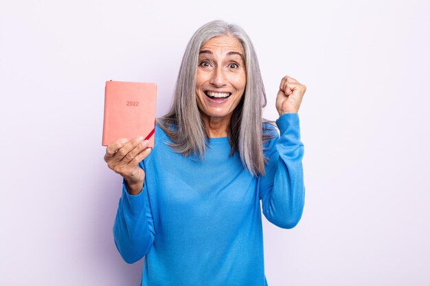 Middle age gray hair woman feeling shocked,laughing and celebrating success. 2022 agenda concept