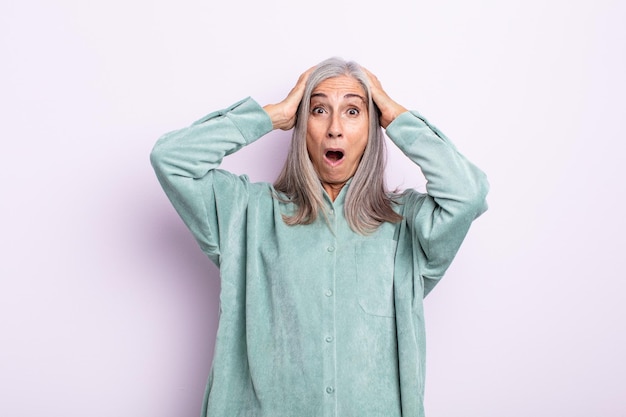 Middle age gray hair woman looking excited and surprised, open-mouthed with both hands on head, feeling like a lucky winner