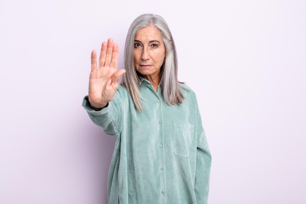 Middle age gray hair woman looking serious, stern, displeased and angry showing open palm making stop gesture