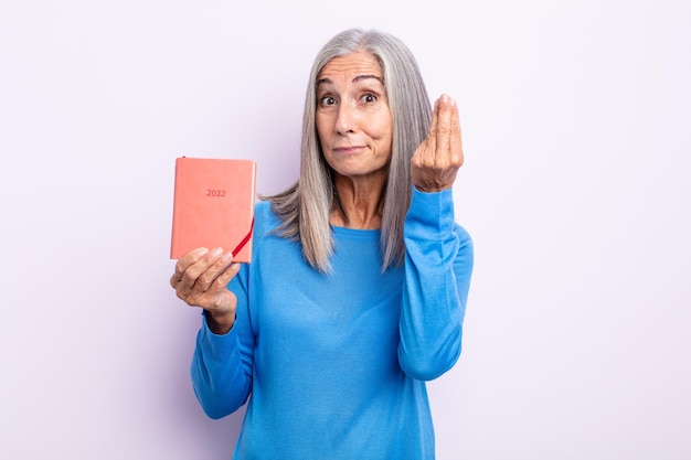 Middle age gray hair woman making capice or money gesture, telling you to pay. 2022 agenda concept