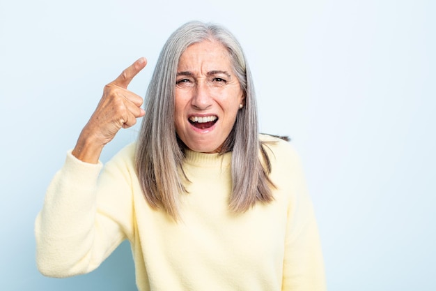 Middle age gray hair woman pointing at camera with an angry aggressive expression looking like a furious, crazy boss