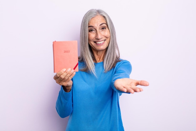 Middle age gray hair woman smiling happily with friendly and offering and showing a concept 2022 agenda concept