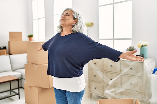 Middle age grey-haired woman smiling happy standing with arms opened at new home.