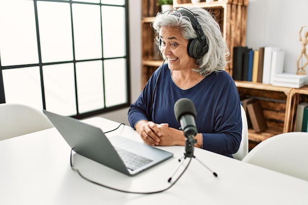 Middle age grey-haired woman smiling happy working at radio studio.