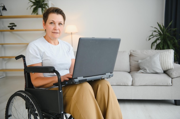 Middle age greyhaired disabled woman having video call sitting on wheelchair at home