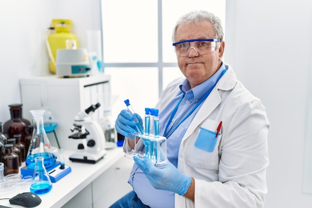 Middle age greyhaired man wearing scientist uniform holding test tube at laboratory