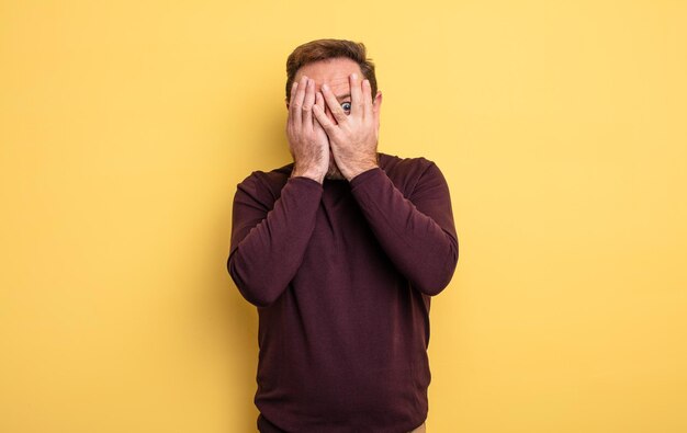 Middle age handsome man feeling scared or embarrassed, peeking or spying with eyes half-covered with hands