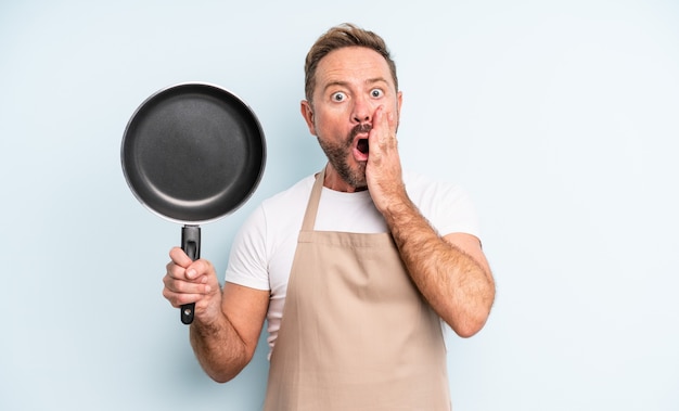 Middle age handsome man feeling shocked and scared. frying pan concept