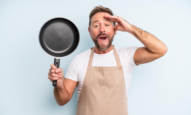 Middle age handsome man looking happy, astonished and surprised. frying pan concept