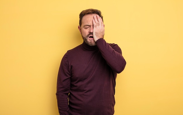 middle age handsome man looking sleepy, bored and yawning, with a headache and one hand covering half the face