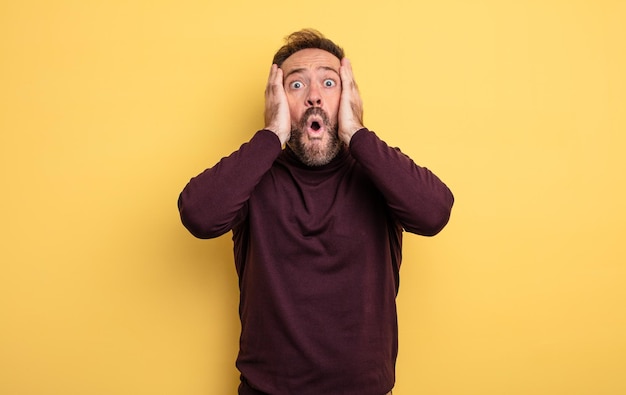 middle age handsome man looking unpleasantly shocked, scared or worried, mouth wide open and covering both ears with hands