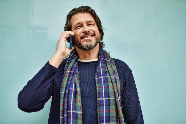 Middle age handsome man speaking on the phone leaning on the wall