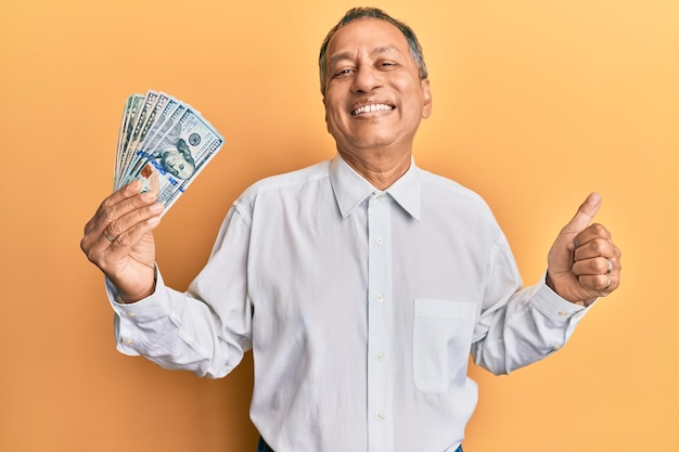 Middle age indian man holding dollars screaming proud celebrating victory and success very excited with raised arm