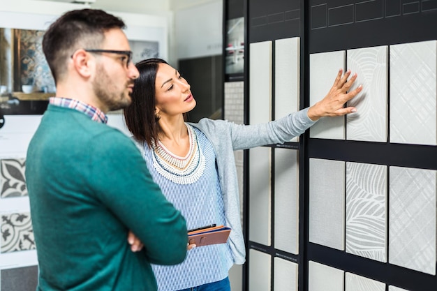 Middle age man choosing ceramic tiles and utensils for his home bathroom and female seller helps him to make right decision